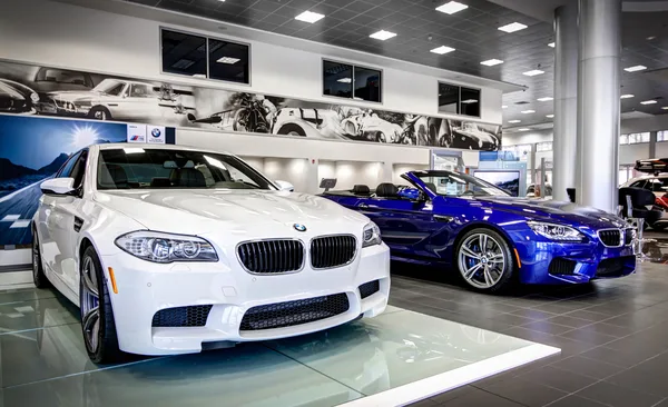 Wide view across a dealership sales floor with desks and vehicles